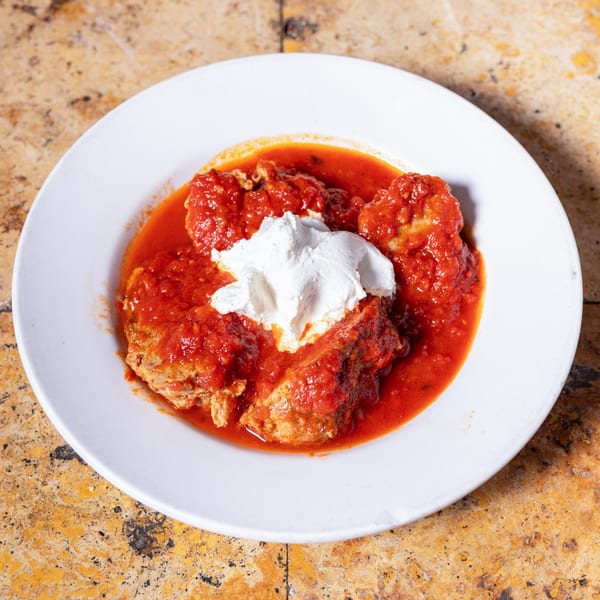Meatballs in rich red tomato sauce topped with a dollop of white ricotta cheese on a white plate.