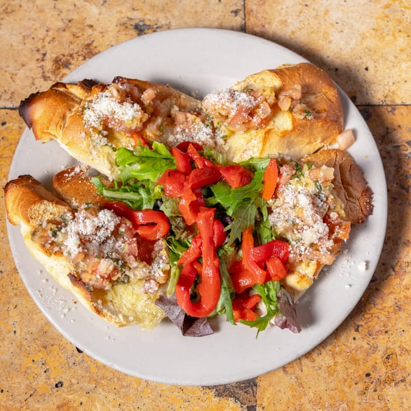 Carmelas bruschetta with diced tomatoes, parmesan, lettuce, and roasted red peppers on a white plate.