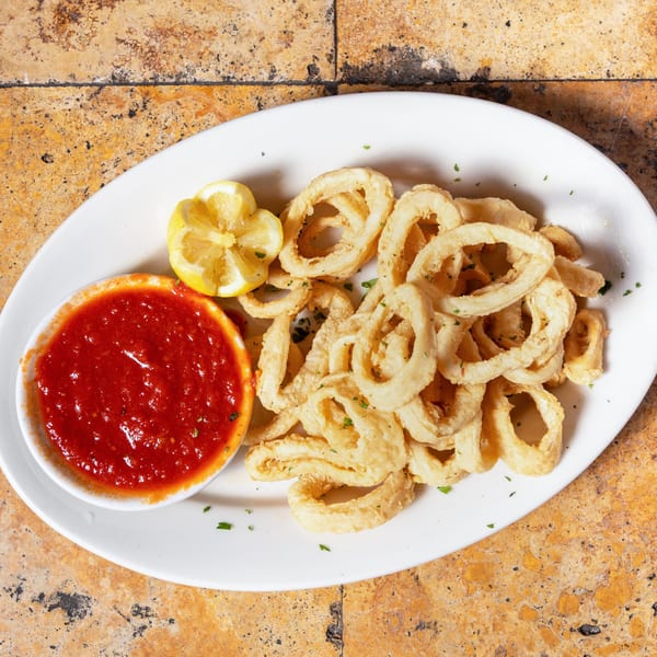 Crispy fried calamari rings with a side of red marinara sauce and lemon wedges on a white plate.