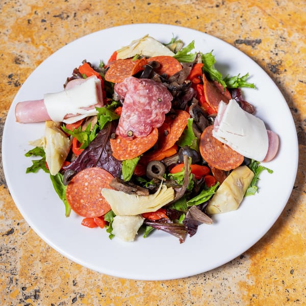 A white plate holds a vibrant Italian antipasto salad with meats, cheeses, artichokes, and olives.