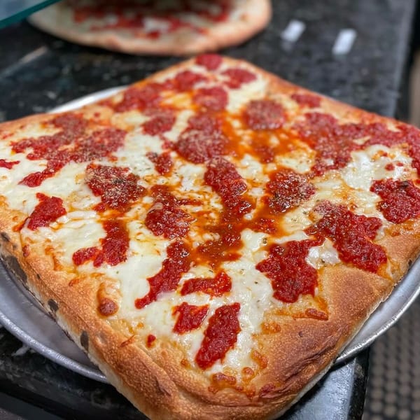 A square Carmelas Brick Oven Pizza with melted mozzarella and dollops of red sauce.