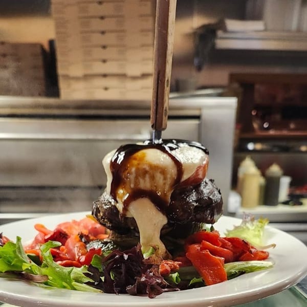 A large burger topped with melted cheese and balsamic glaze, served with a side salad.