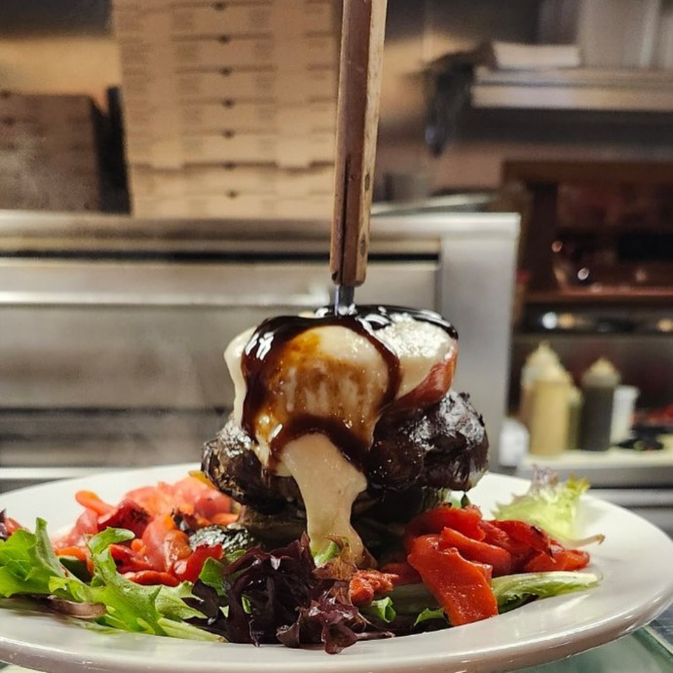 A large burger topped with melted cheese and balsamic glaze, served with a side salad.