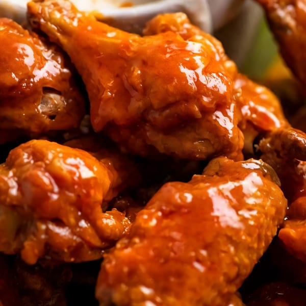 Close-up of several chicken wings coated in a glistening orange buffalo sauce, ready to be served.